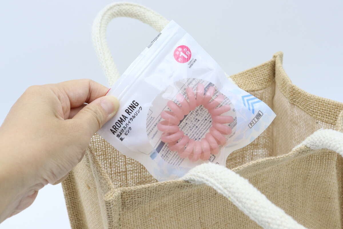 ジュート素材のバッグにダイソー虫よけスパイラルリングのパッケージを入れる手。 ジュート素材のバッグにダイソー虫よけスパイラルリングのパッケージを入れる手。