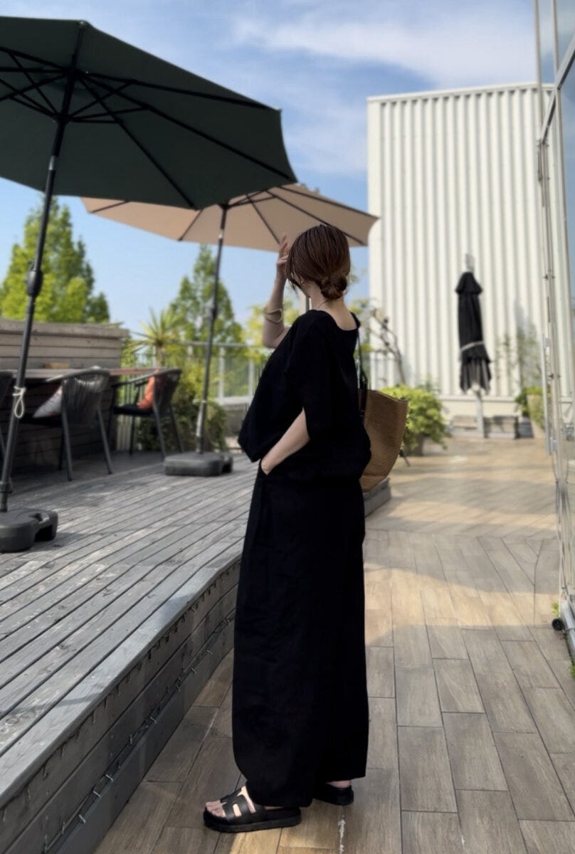 黒いリネンセットアップの女性が屋外テラスで横向きに立つ 黒いリネンセットアップの女性が屋外テラスで横向きに立つ