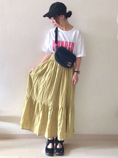 白のロゴTに黄色のマキシスカートを履いた女性