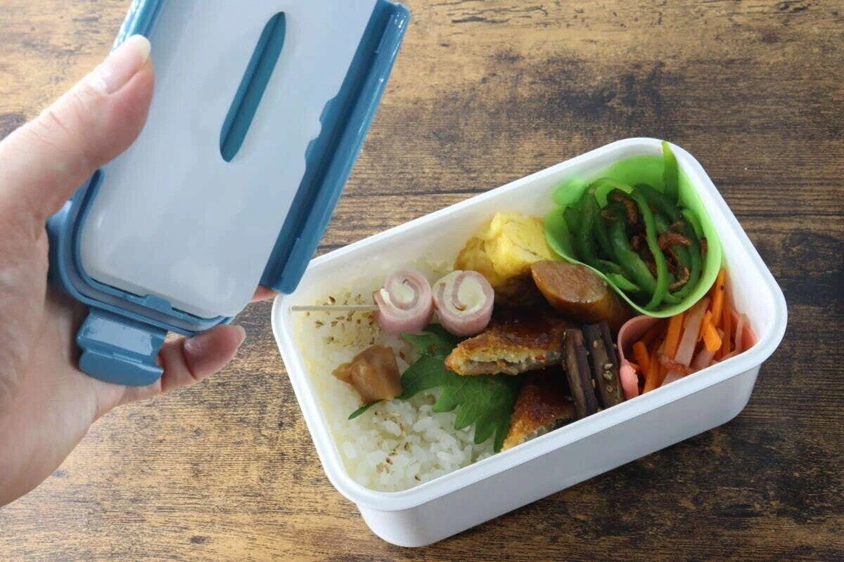 青い蓋の弁当箱を開け、保冷剤付きの蓋と中のおかずを見せている