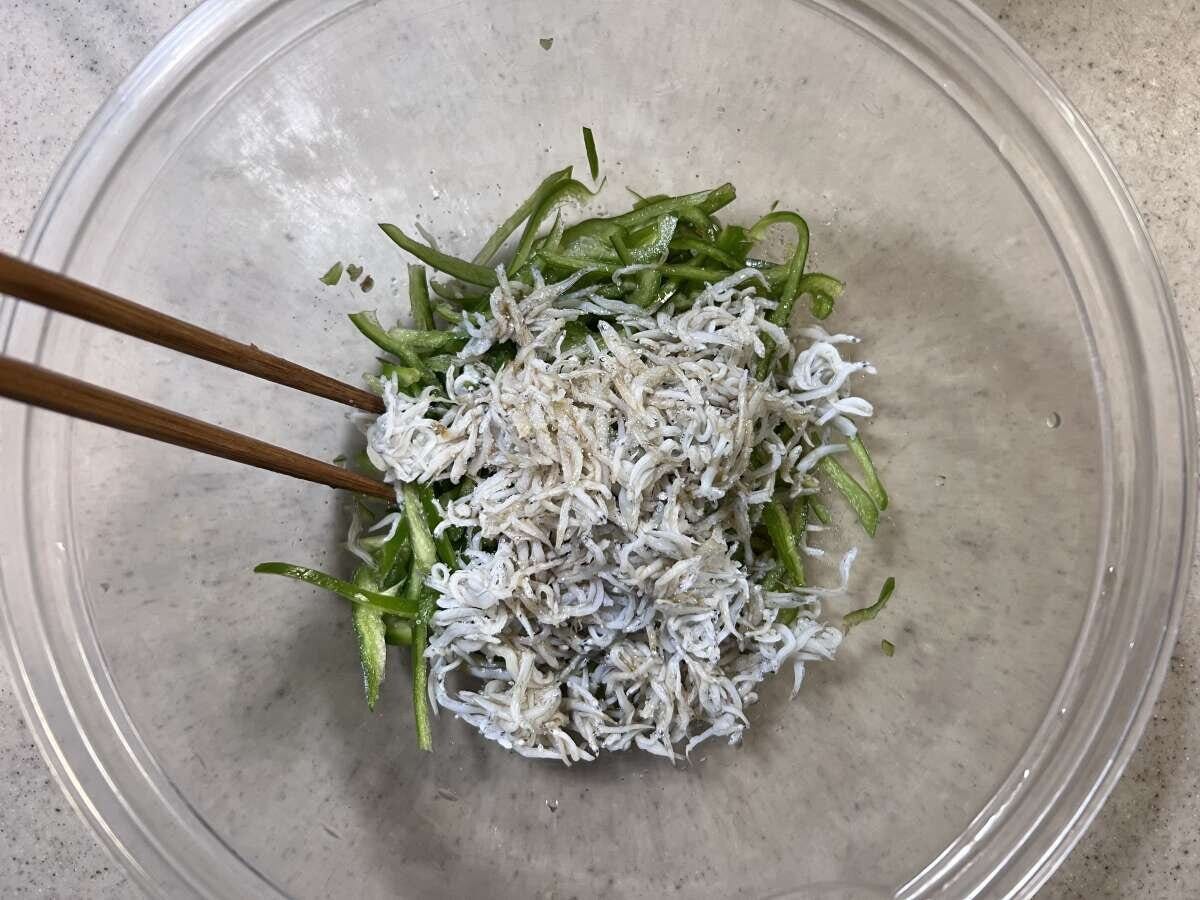 透明なボウルで千切りピーマンとしらす、調味料を箸で混ぜている