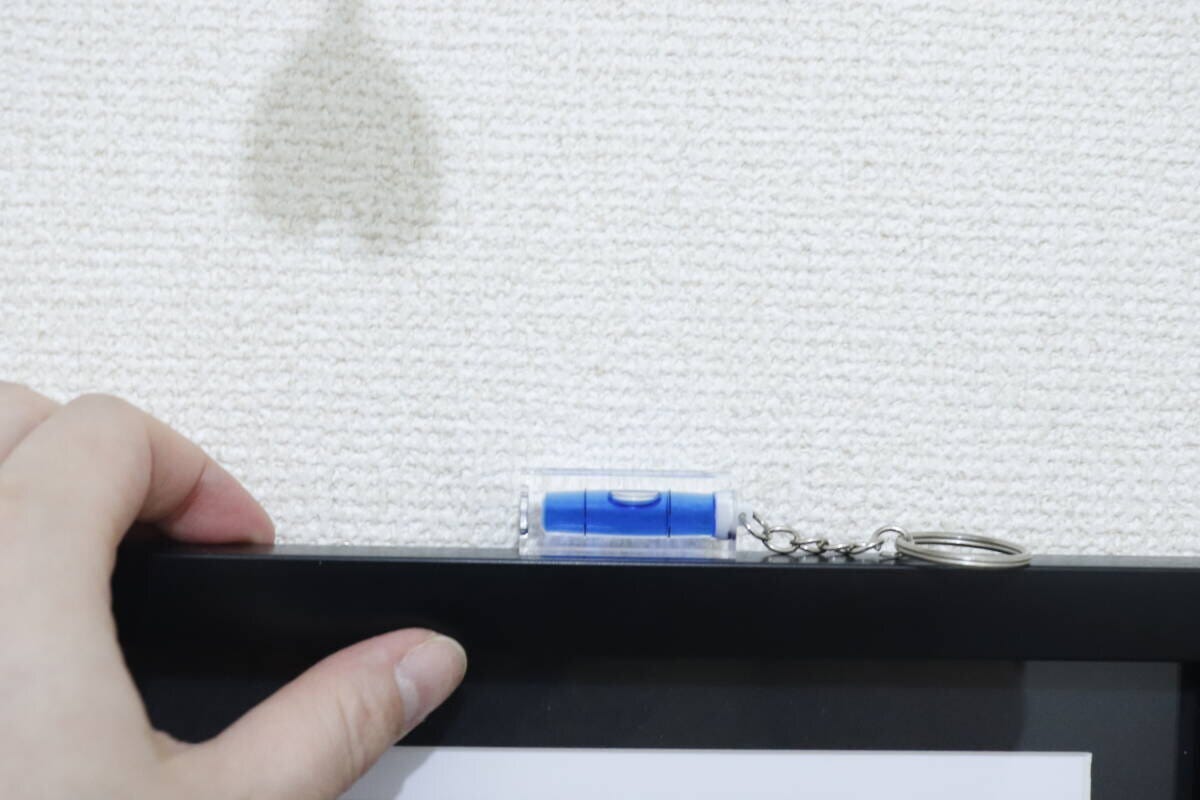 額縁の縁に置かれたキーホルダー水平器と手を添えている