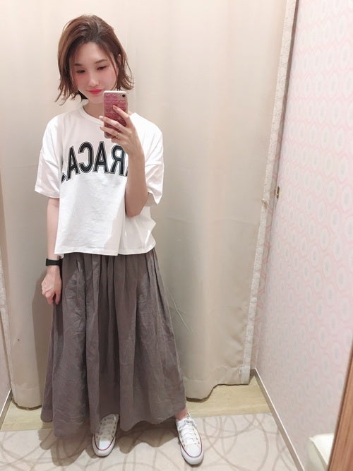 白のロゴTにベージュのギャザースカートを履いた女性