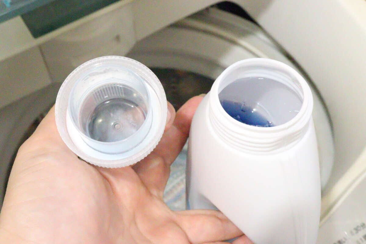 右手が持っている計量カップの蓋と、左手で持っている液体洗剤ボトルの口元が写っている