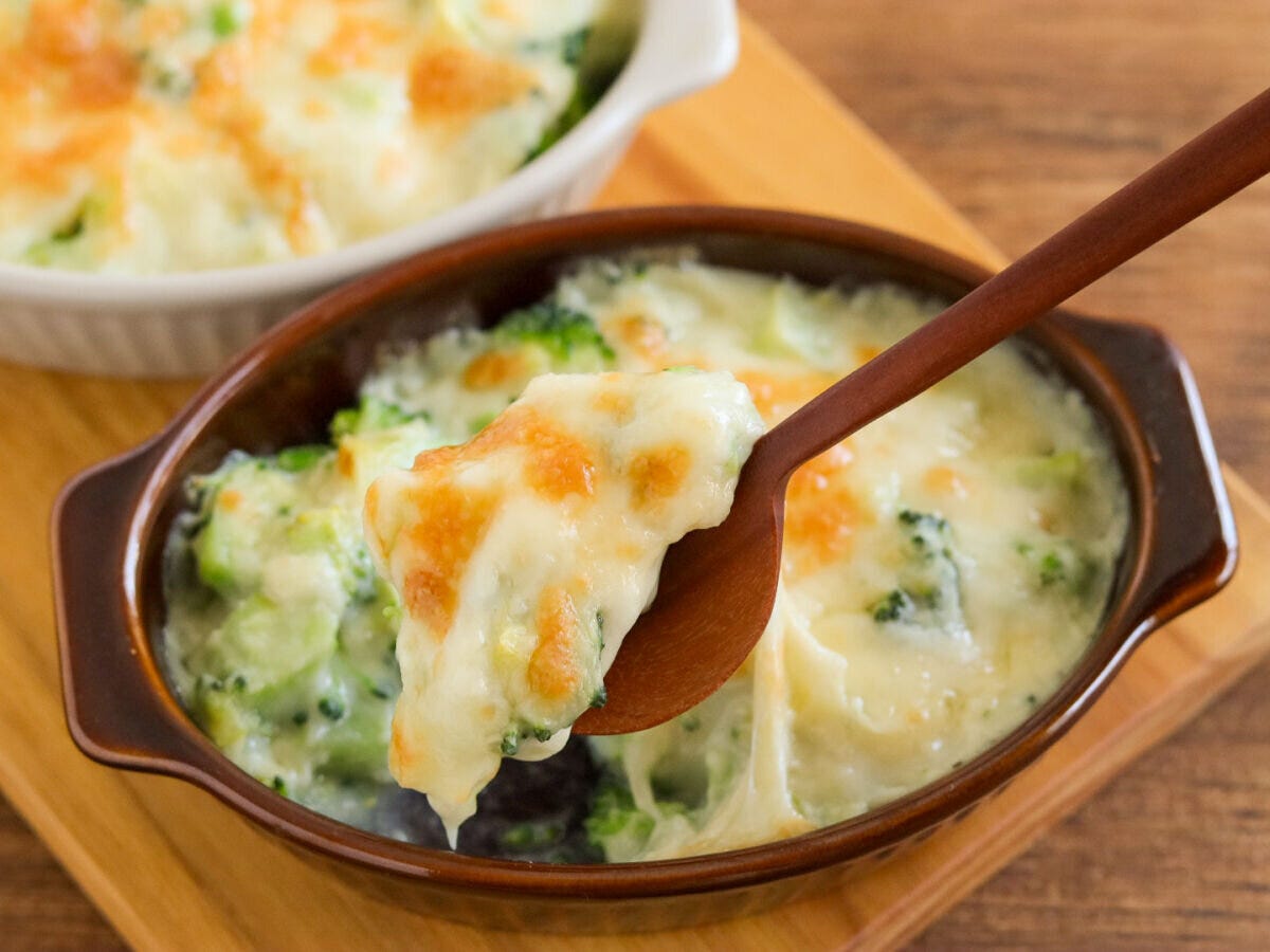 茶色のグラタン皿のブロッコリーグラタンを木のスプーンですくいチーズがとろりと伸びている様子 茶色のグラタン皿のブロッコリーグラタンを木のスプーンですくいチーズがとろりと伸びている様子