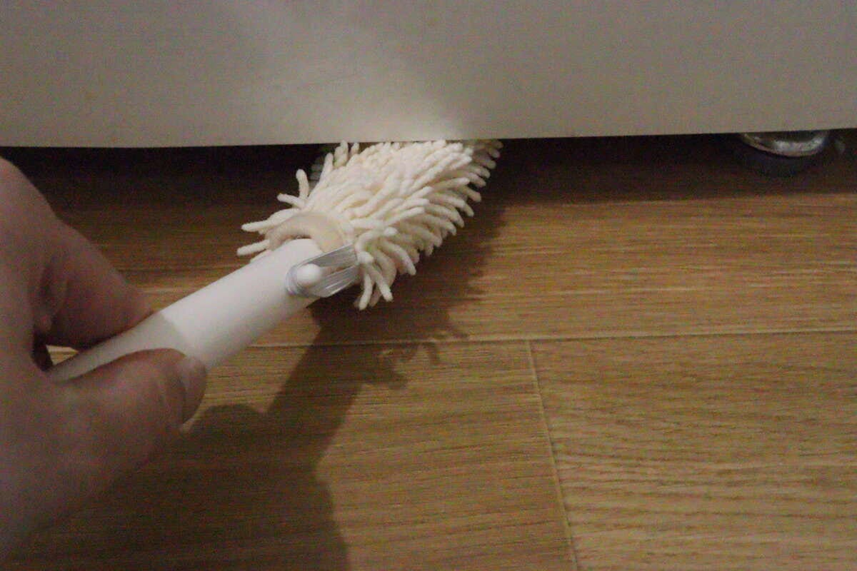 冷蔵庫の下の狭い隙間をハンディモップで掃除する手元