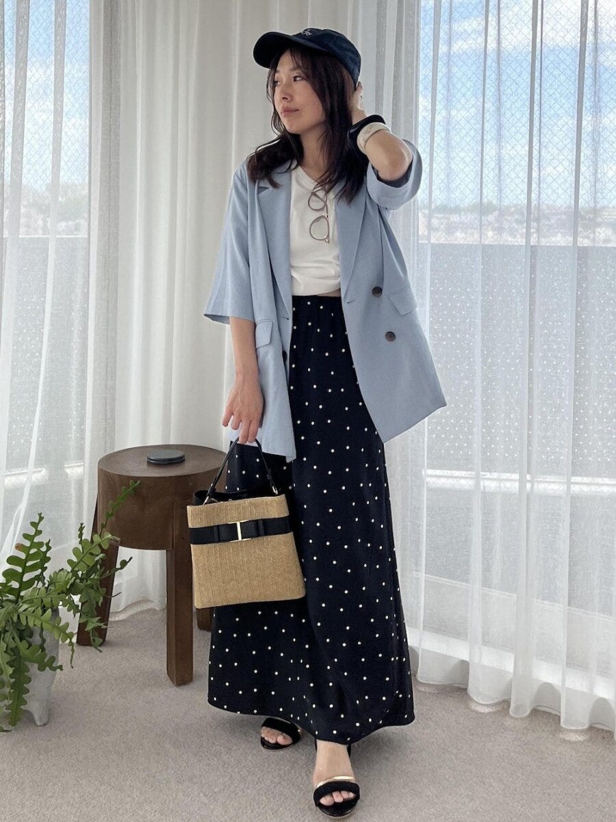 黒ドット柄スカートに水色ジャケットとキャップを被った女性