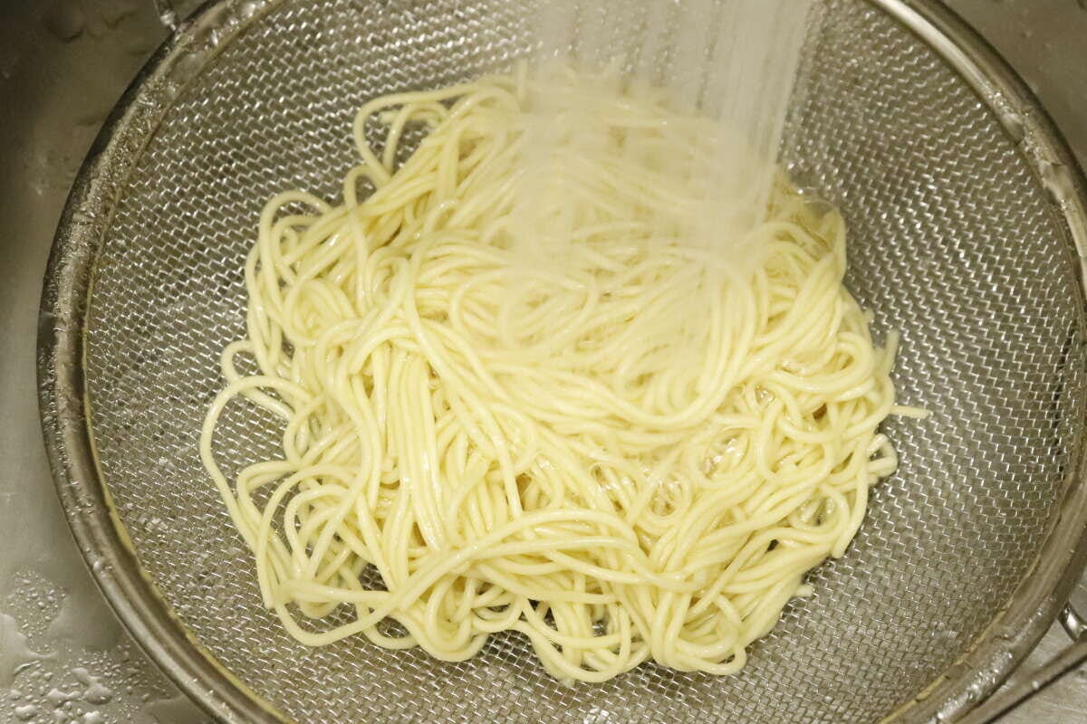 シンクで浅型ザルを使いラーメンのような麺を湯切りしている様子