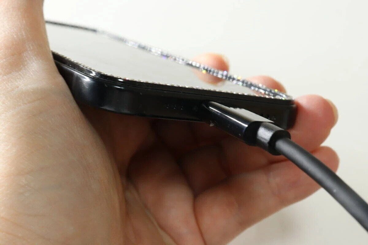 黒いスマホの側面の端子にケーブルを差し込んでいる手元のアップ