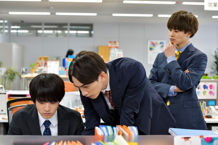 仕事中の安達(赤楚衛二)と黒沢(町田啓太)、2人を見つめる六角(草川拓弥/超特急) (C)豊田悠/SQUARE ENIX・「30 歳まで童貞だと魔法使いになれるらしい」製作委員会