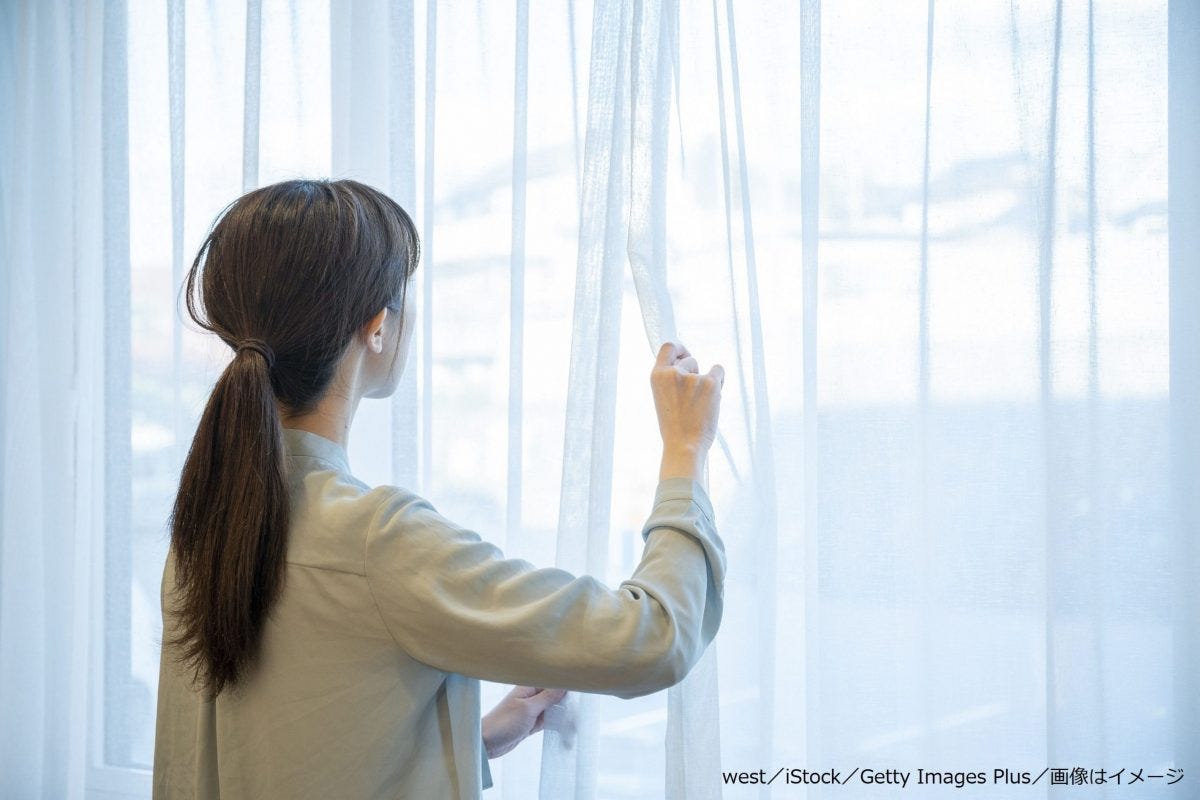 レースのカーテンを開ける女性