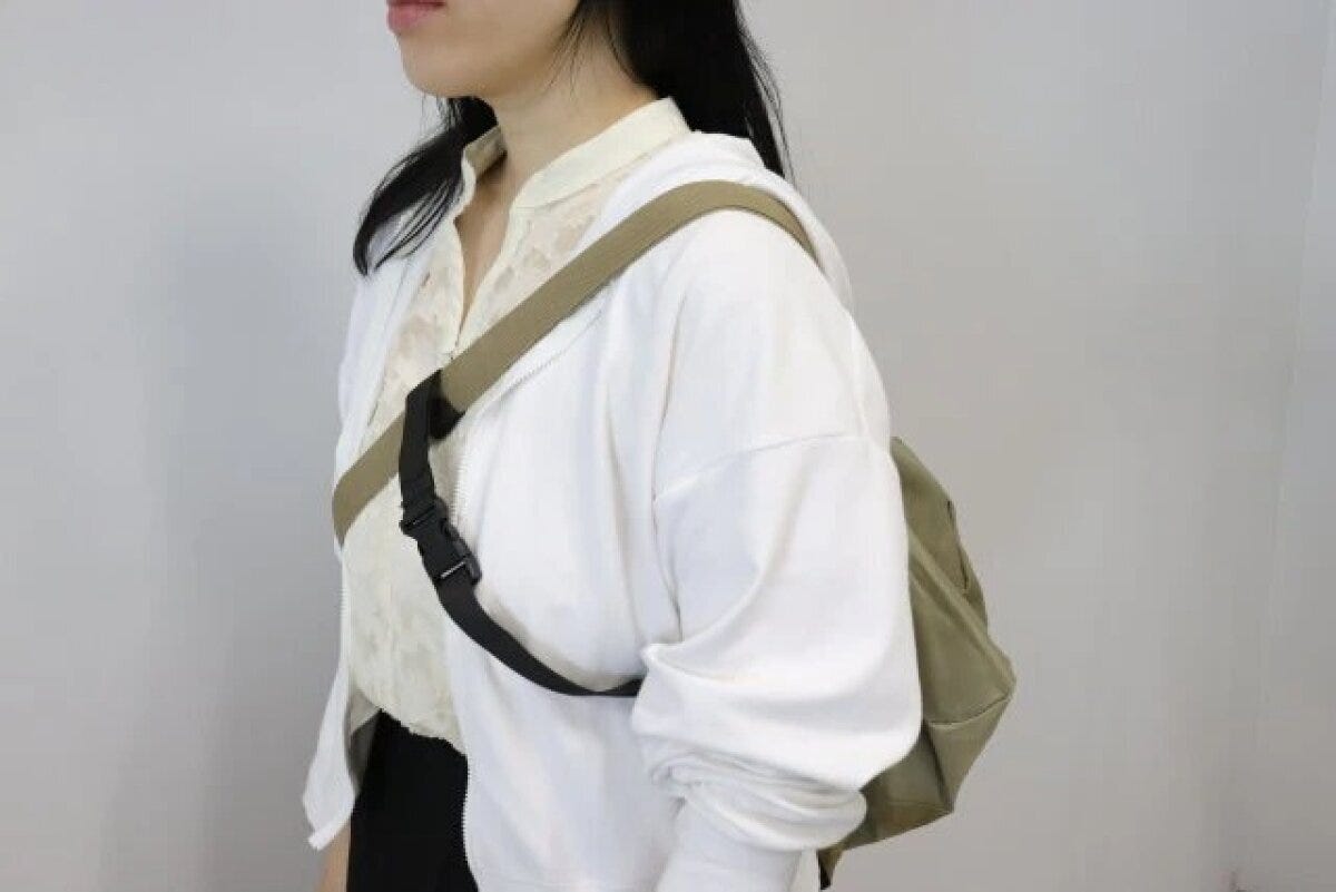 女性がカーキ色のショルダーバッグを肩にかけ、黒いクロスストラップで固定している横向きの姿 女性がカーキ色のショルダーバッグを肩にかけ、黒いクロスストラップで固定している横向きの姿