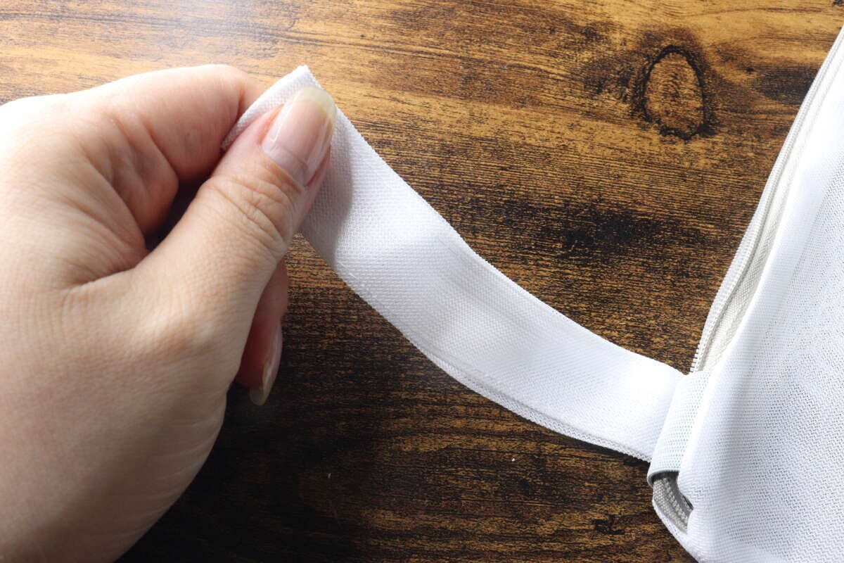女性の手が白い洗濯ネットの吊り下げループをつまんで見せている