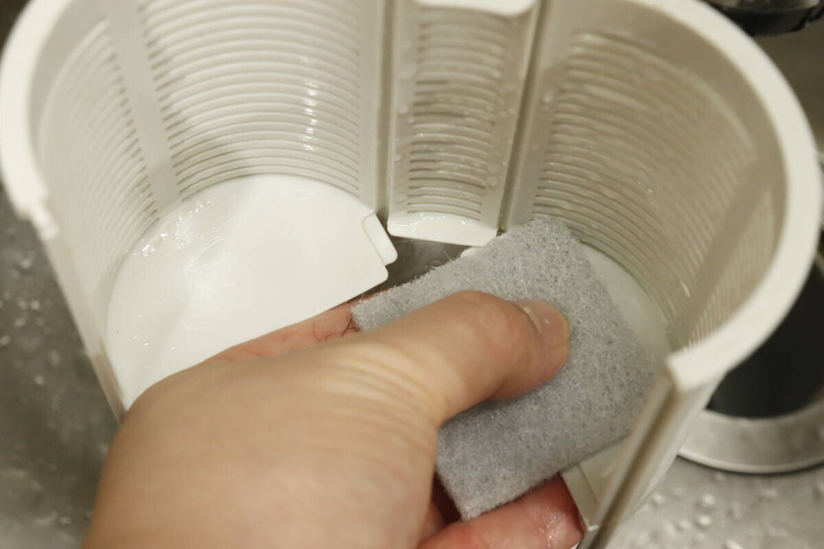 排水溝の白いプラスチック製パーツをスポンジで洗っている 排水溝の白いプラスチック製パーツをスポンジで洗っている