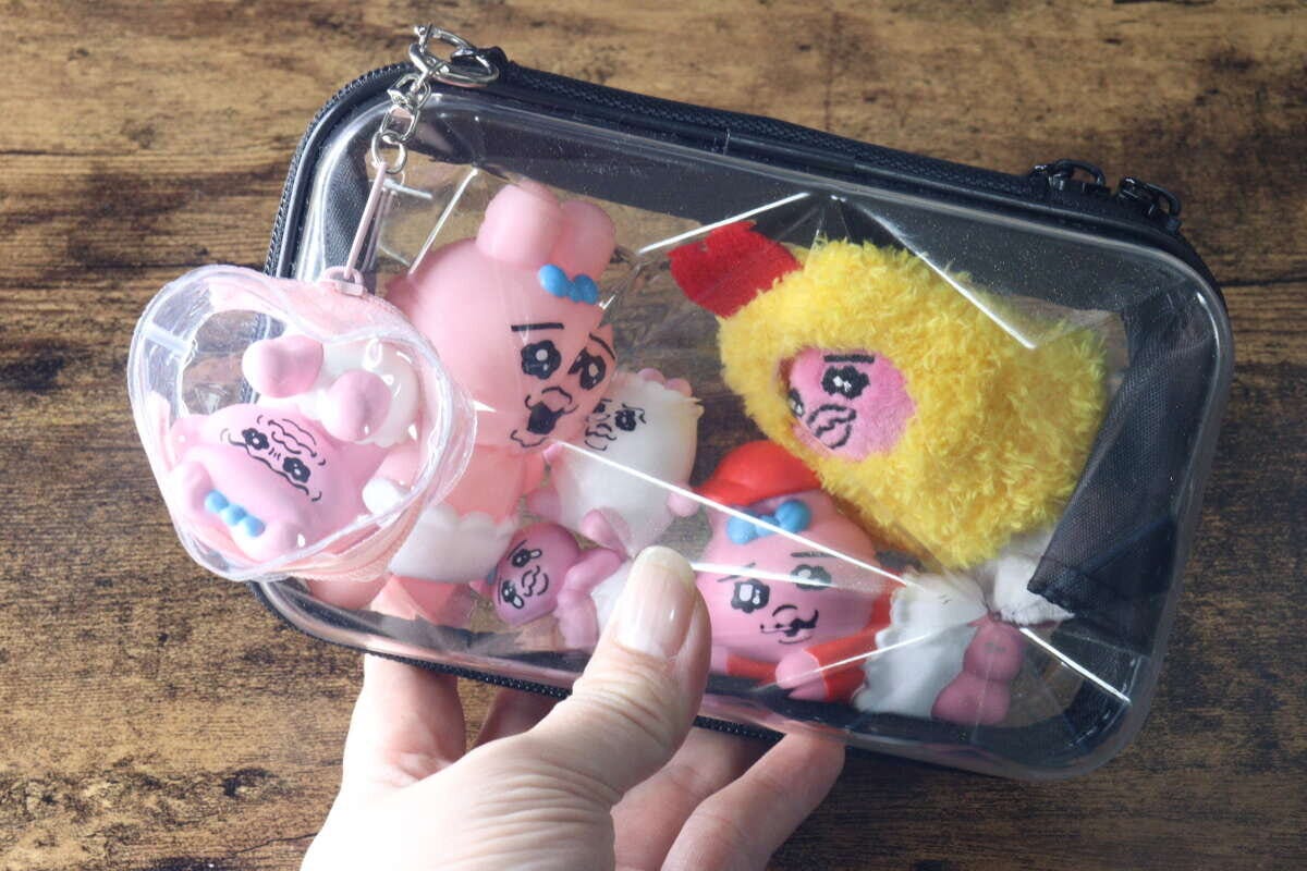 女性の手が透明なダイヤモンド形収納バッグを持ち、中にキャラクターのぬいぐるみが複数入っている 女性の手が透明なダイヤモンド形収納バッグを持ち、中にキャラクターのぬいぐるみが複数入っている