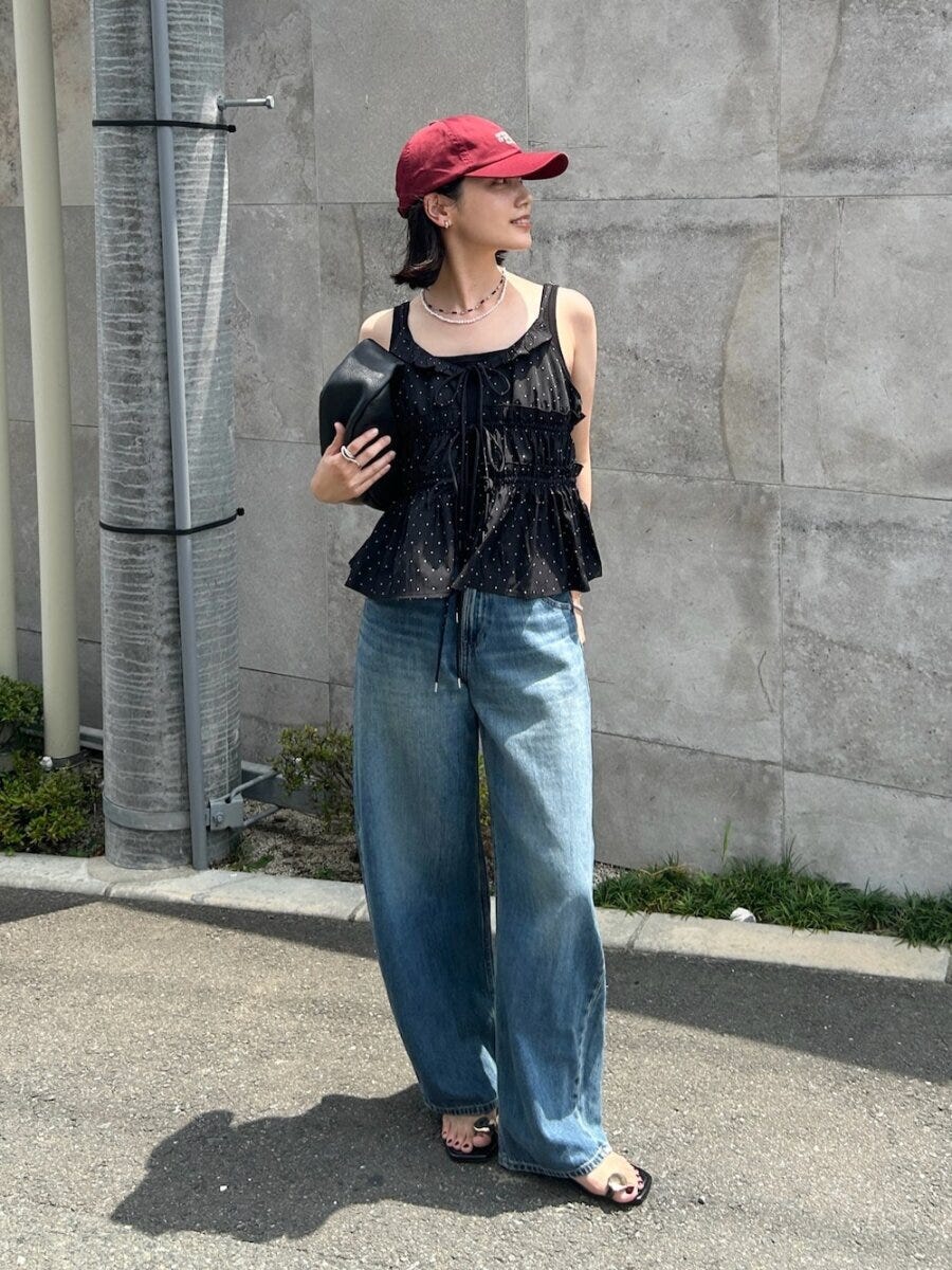 赤いキャップと黒いドット柄キャミソール、ワイドデニムを着用した女性がバッグを持ち横を向いて立っている