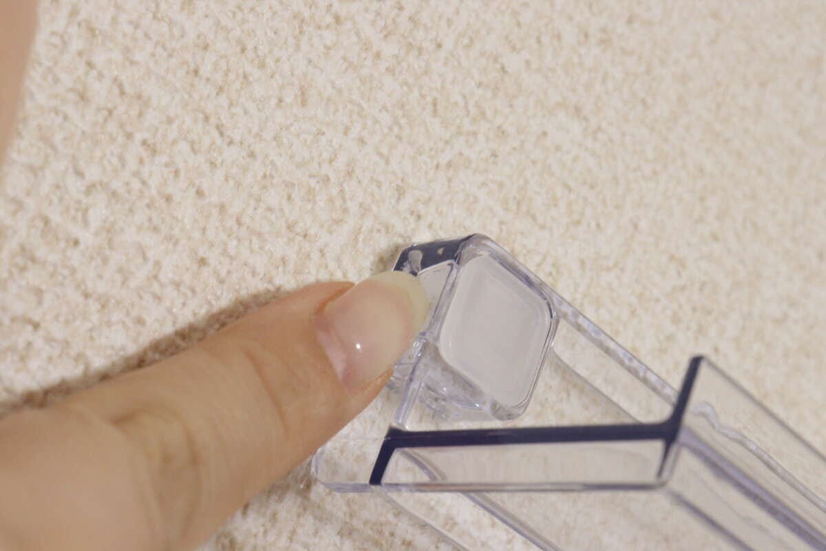 壁に設置した透明な棚の角を指でしっかりと押さえて固定している様子 壁に設置した透明な棚の角を指でしっかりと押さえて固定している様子