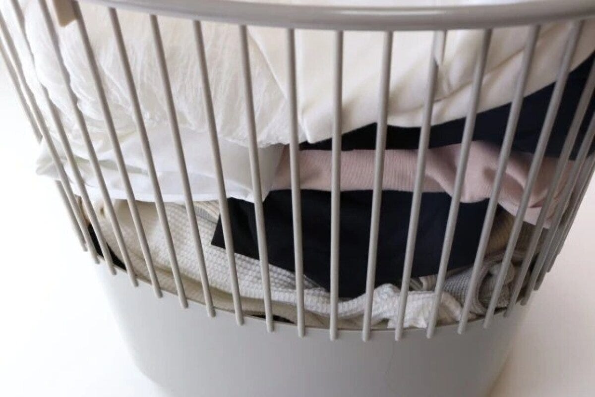 白いワイヤーバスケットの中に、たたまれた洗濯物や衣類がたっぷり入っている 白いワイヤーバスケットの中に、たたまれた洗濯物や衣類がたっぷり入っている