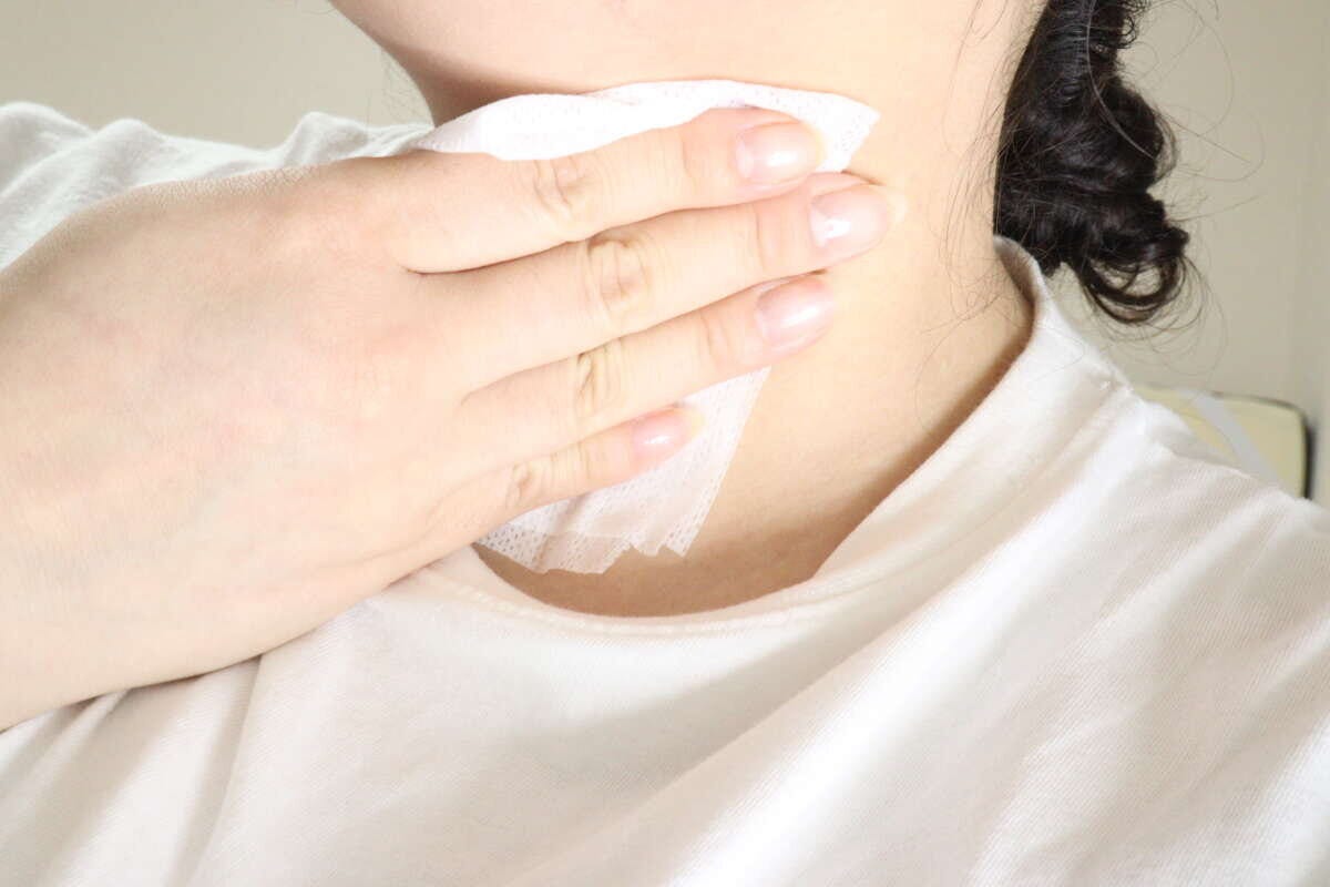 女性が首元をボディシートで拭いて、さっぱりしている様子
