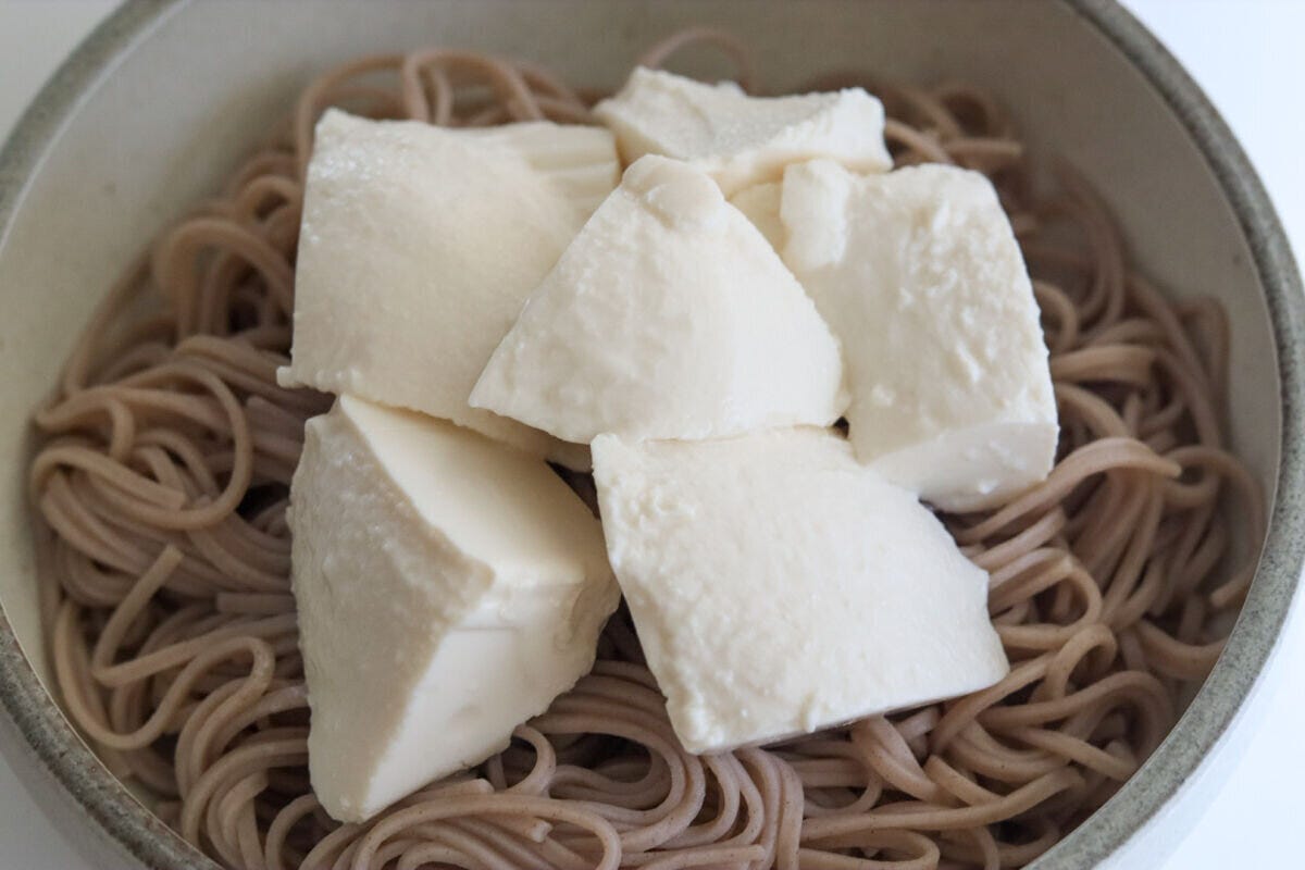そばの上に大きく崩してのせられた白い絹ごし豆腐