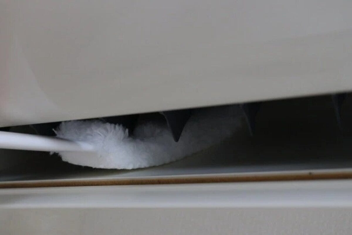 エアコンの送風口の狭い隙間を、白いクリーナーで掃除している エアコンの送風口の狭い隙間を、白いクリーナーで掃除している