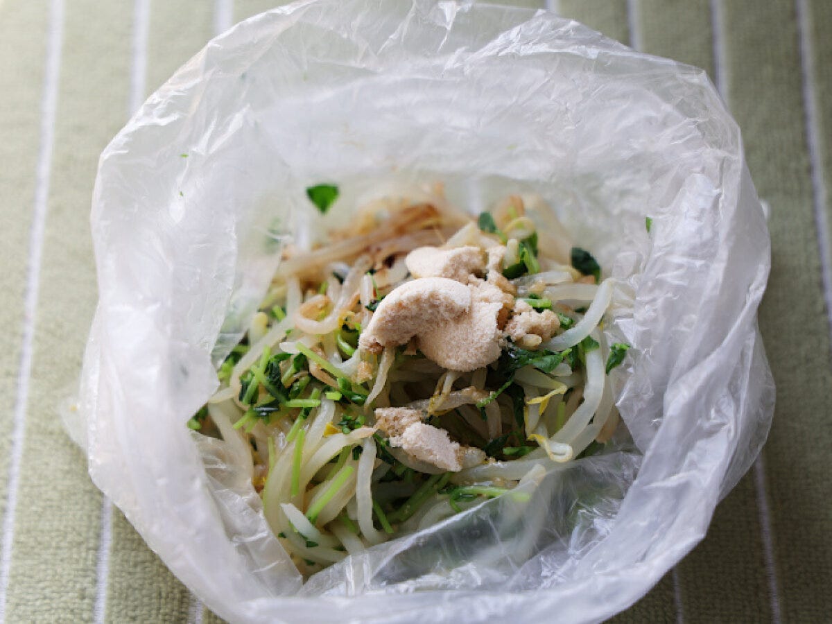 水分を絞ったもやしと豆苗の入ったビニール袋に、白い顆粒状の中華スープの素などの調味料を加えたところ