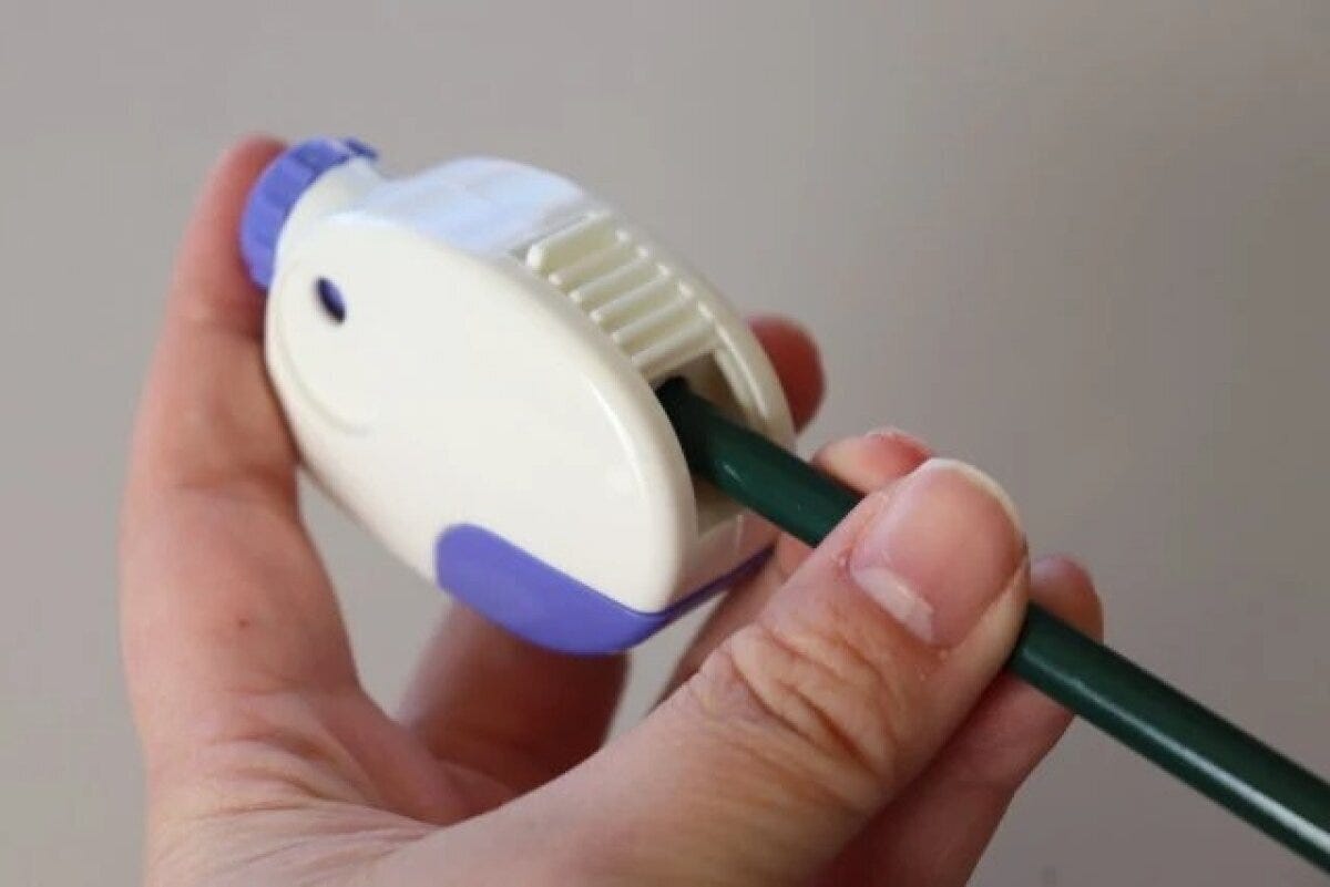 手が白と紫の鉛筆削りで緑色の鉛筆を削っている