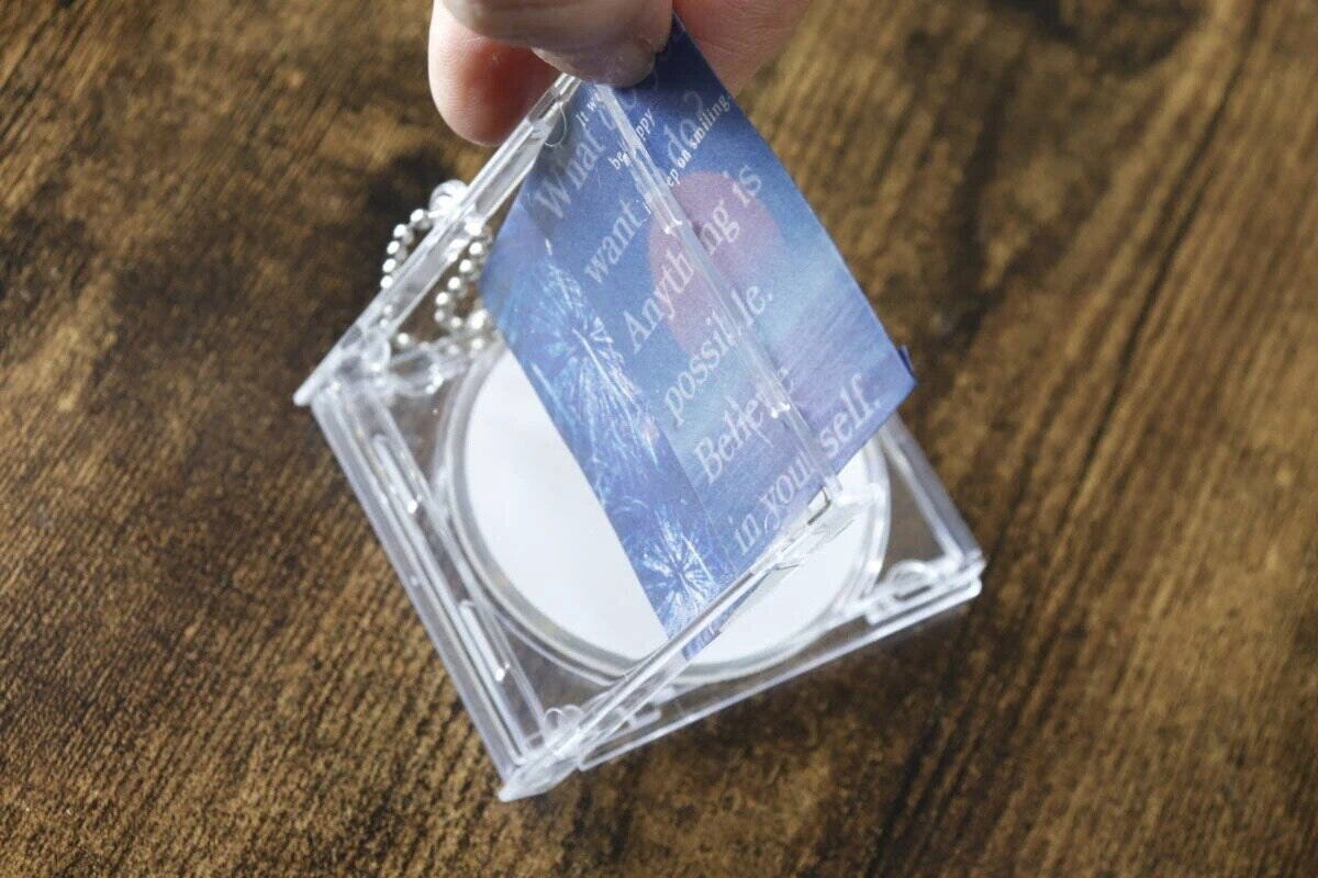透明なCDケース型キーホルダーに、女性が青い紙を挟み込んでいる 透明なCDケース型キーホルダーに、女性が青い紙を挟み込んでいる