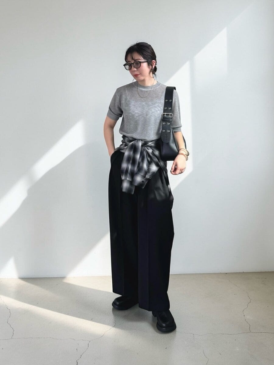 グレーニットと黒ワイドパンツにチェックシャツを腰巻きした女性