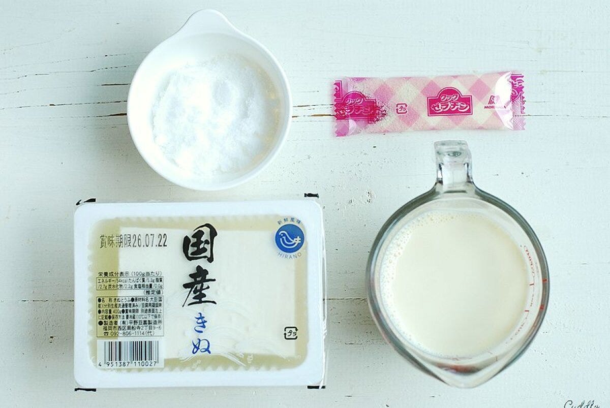 白い木目のテーブルに絹ごし豆腐、豆乳、砂糖、粉ゼラチンが並べられた俯瞰写真
