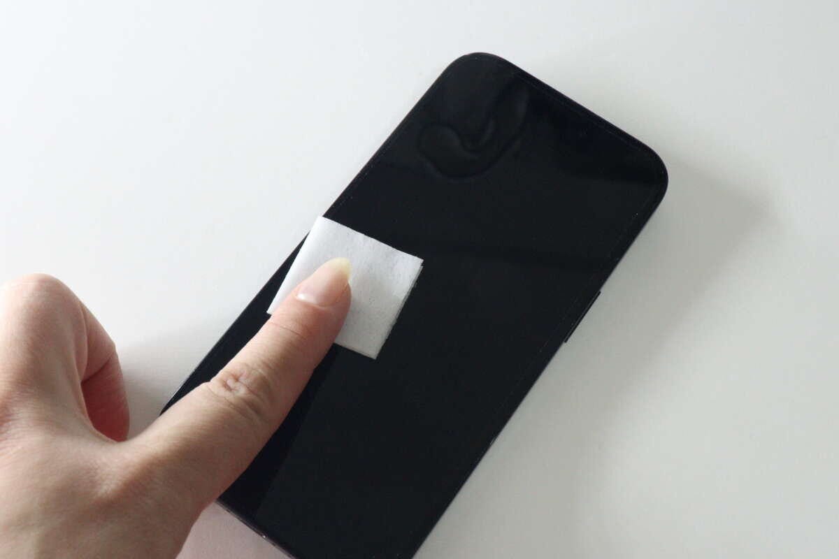 女性の手がスマホ画面をウェットシートで拭いている様子 女性の手がスマホ画面をウェットシートで拭いている様子