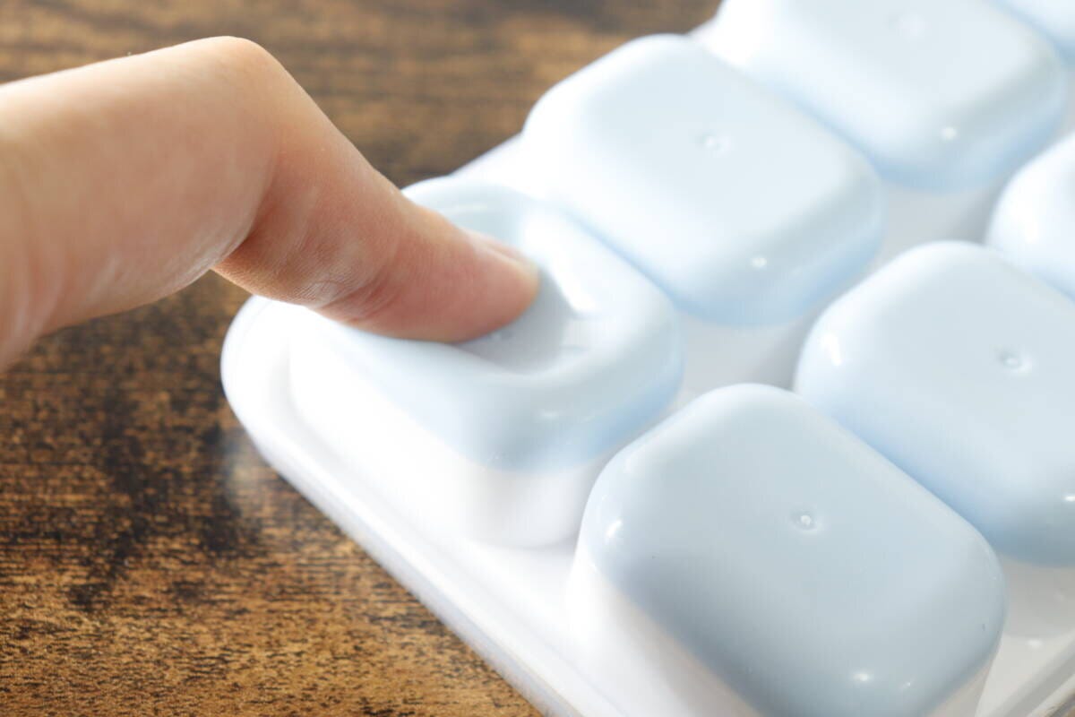 人差し指でアイストレーの底にある柔らかい部分を押し、氷を外そうとしている手のアップ 人差し指でアイストレーの底にある柔らかい部分を押し、氷を外そうとしている手のアップ