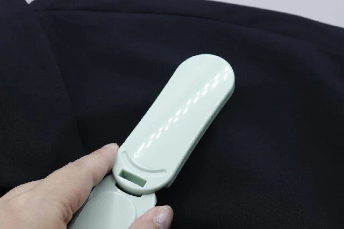 黒い服の表面を薄緑色の洋服ブラシでブラッシングしている様子