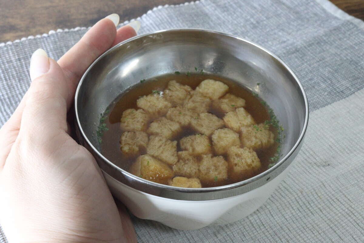 温かいスープを注いだ二重構造のボウルを女性の手で持ちながら食卓に置いている様子 温かいスープを注いだ二重構造のボウルを女性の手で持ちながら食卓に置いている様子