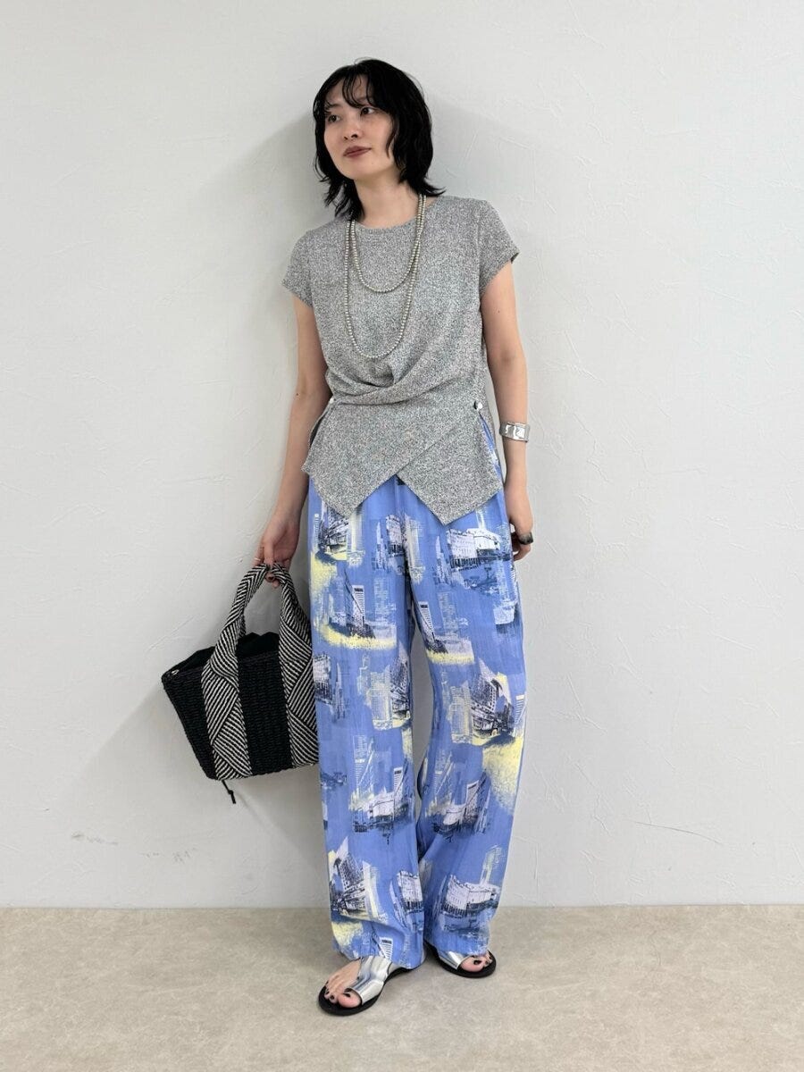 グレーのトップスと青いプリント柄パンツの女性