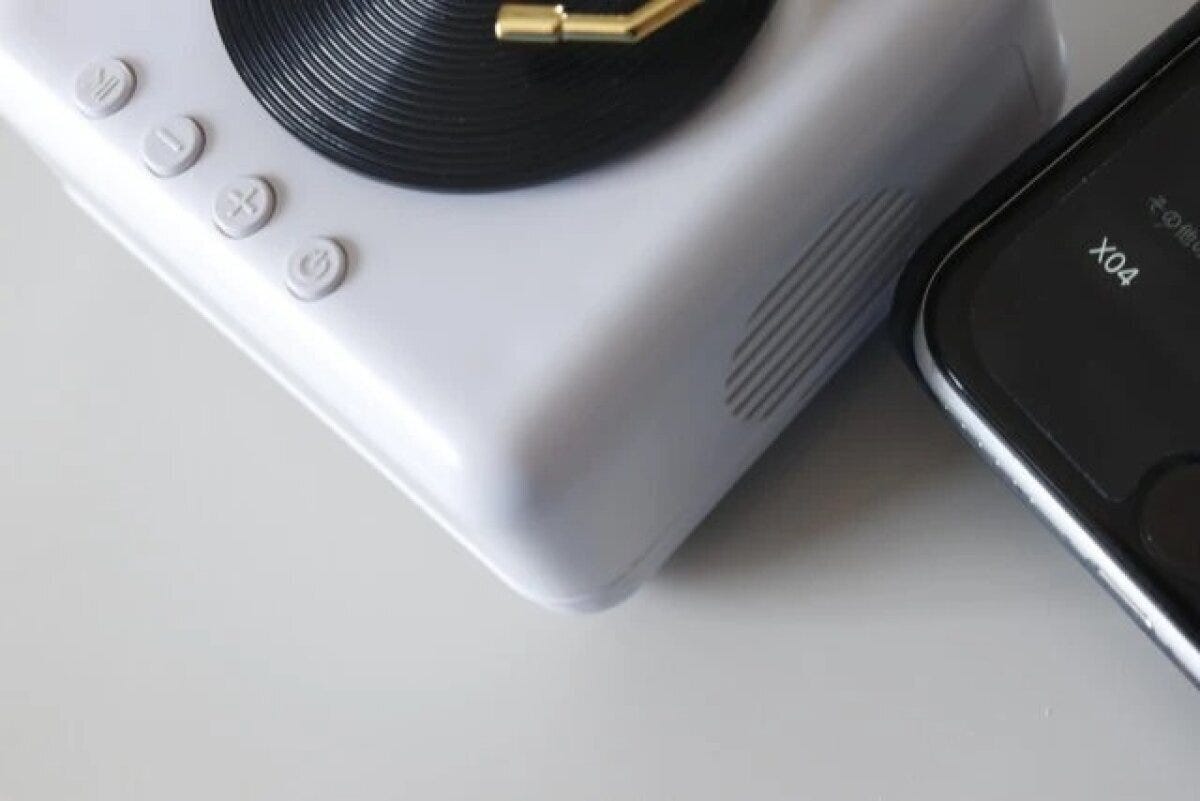 白いレコードプレーヤー型スピーカーの横にスマートフォンが置かれ、Bluetooth接続画面が見える