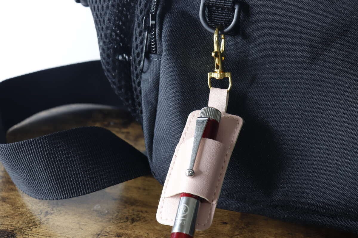 赤いペンを差したペンホルダーを黒いバッグに吊り下げている 赤いペンを差したペンホルダーを黒いバッグに吊り下げている