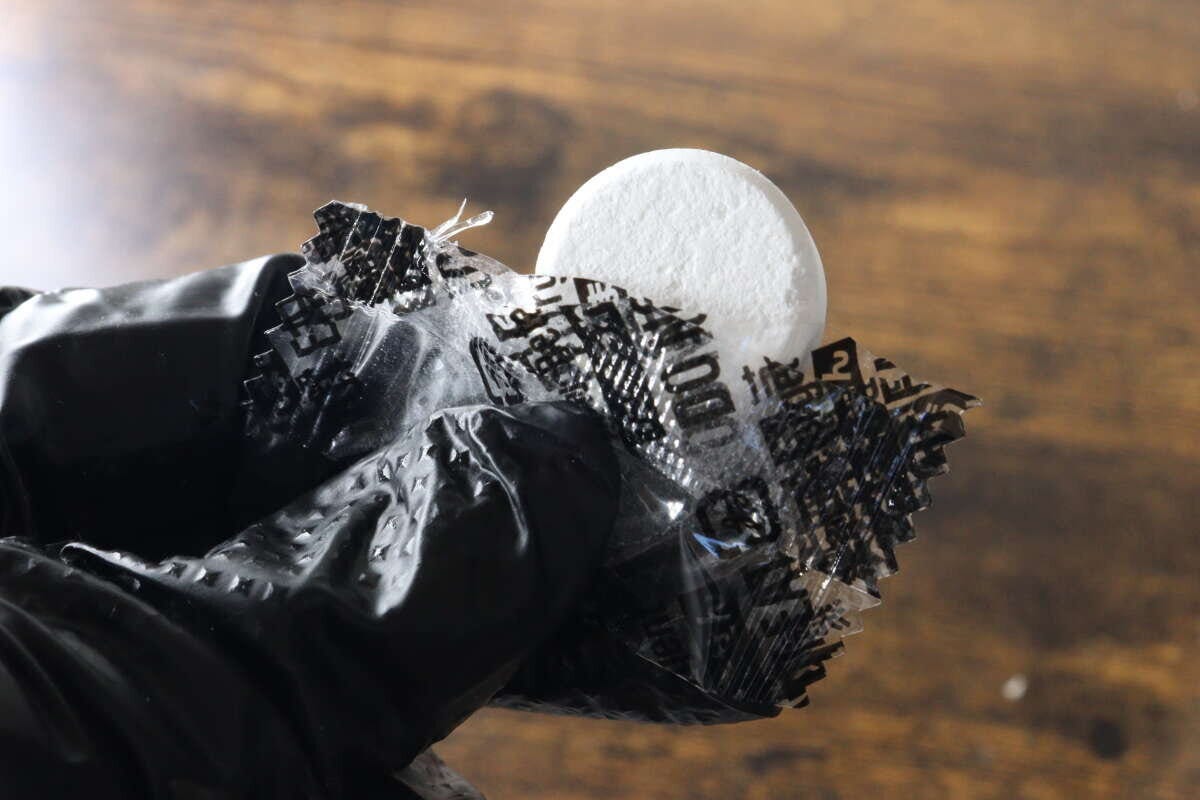 黒い手袋をした手で個包装から白い錠剤を取り出している状態 黒い手袋をした手で個包装から白い錠剤を取り出している状態