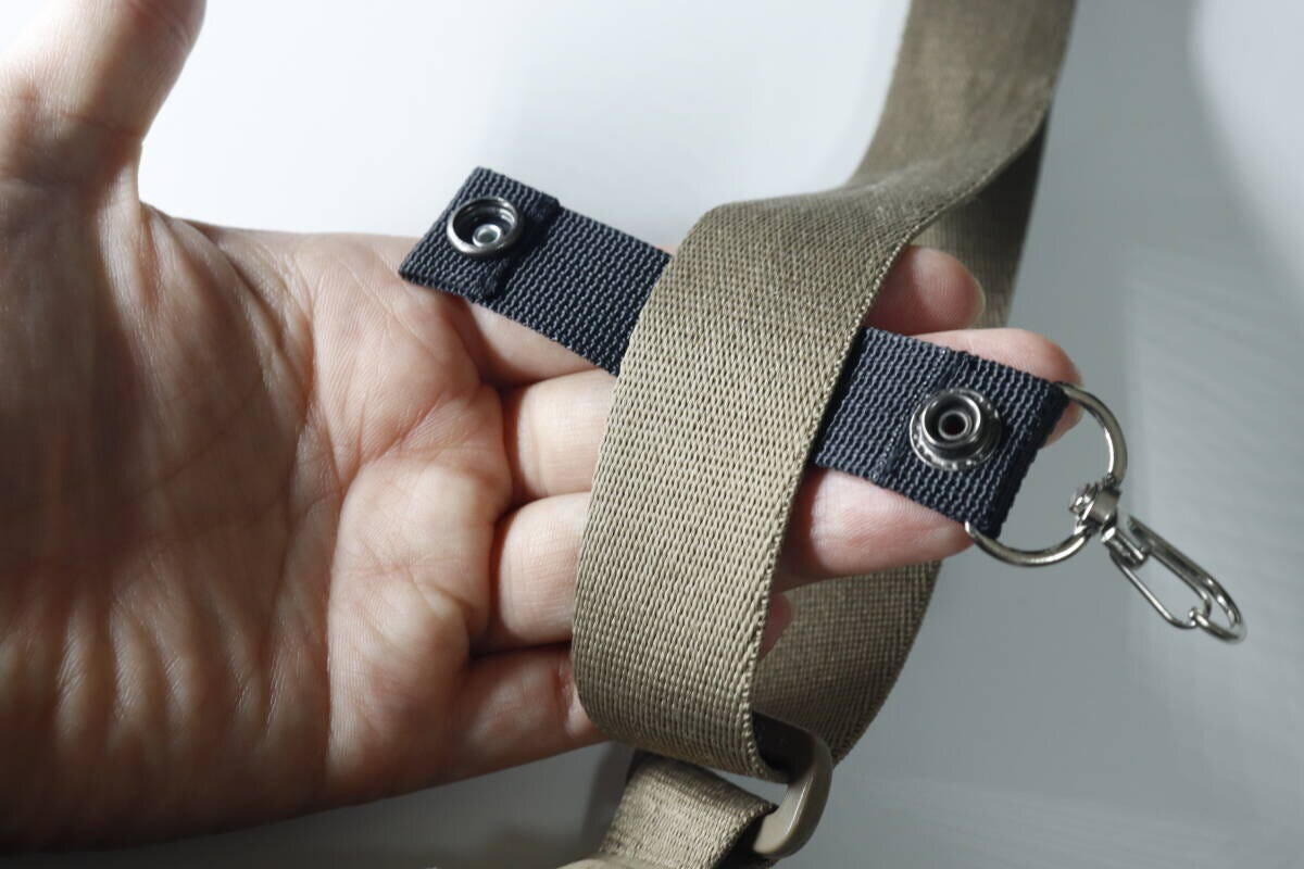 手でバッグの太いベルトに小物ホルダーを巻きつけスナップボタンを留める様子