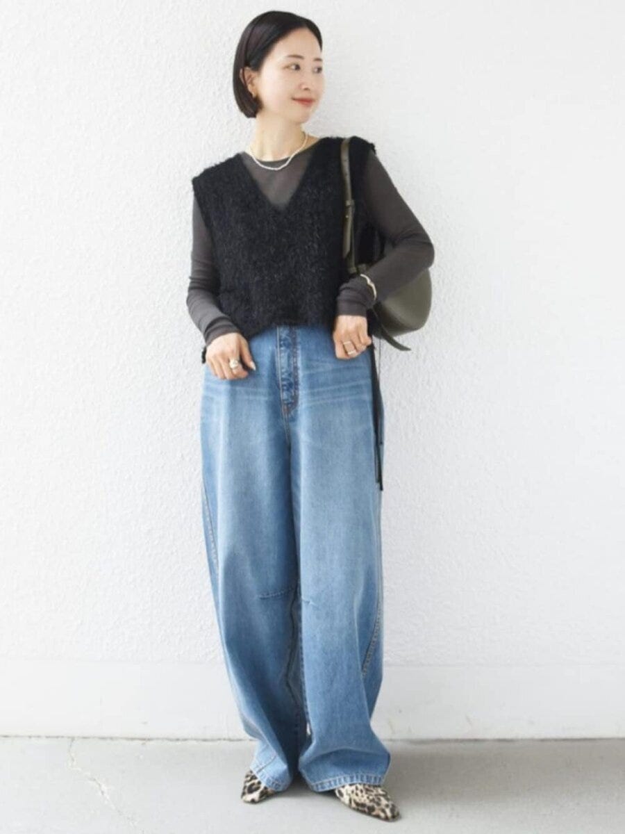 黒いフェザーベストとシアーカットソーを着こなすショートヘアの女性