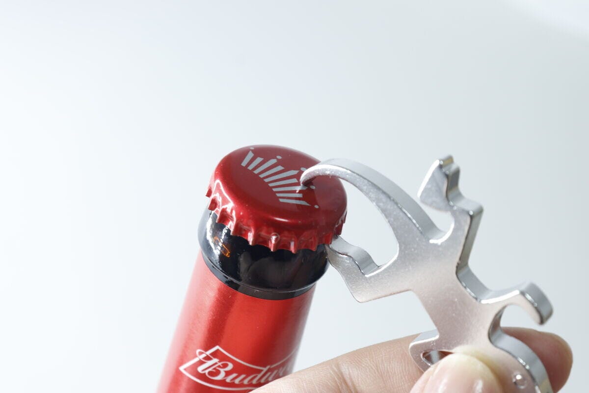 人の指が銀色のトカゲ型栓抜きキーホルダーで赤い瓶ビールの蓋を開けようとしている