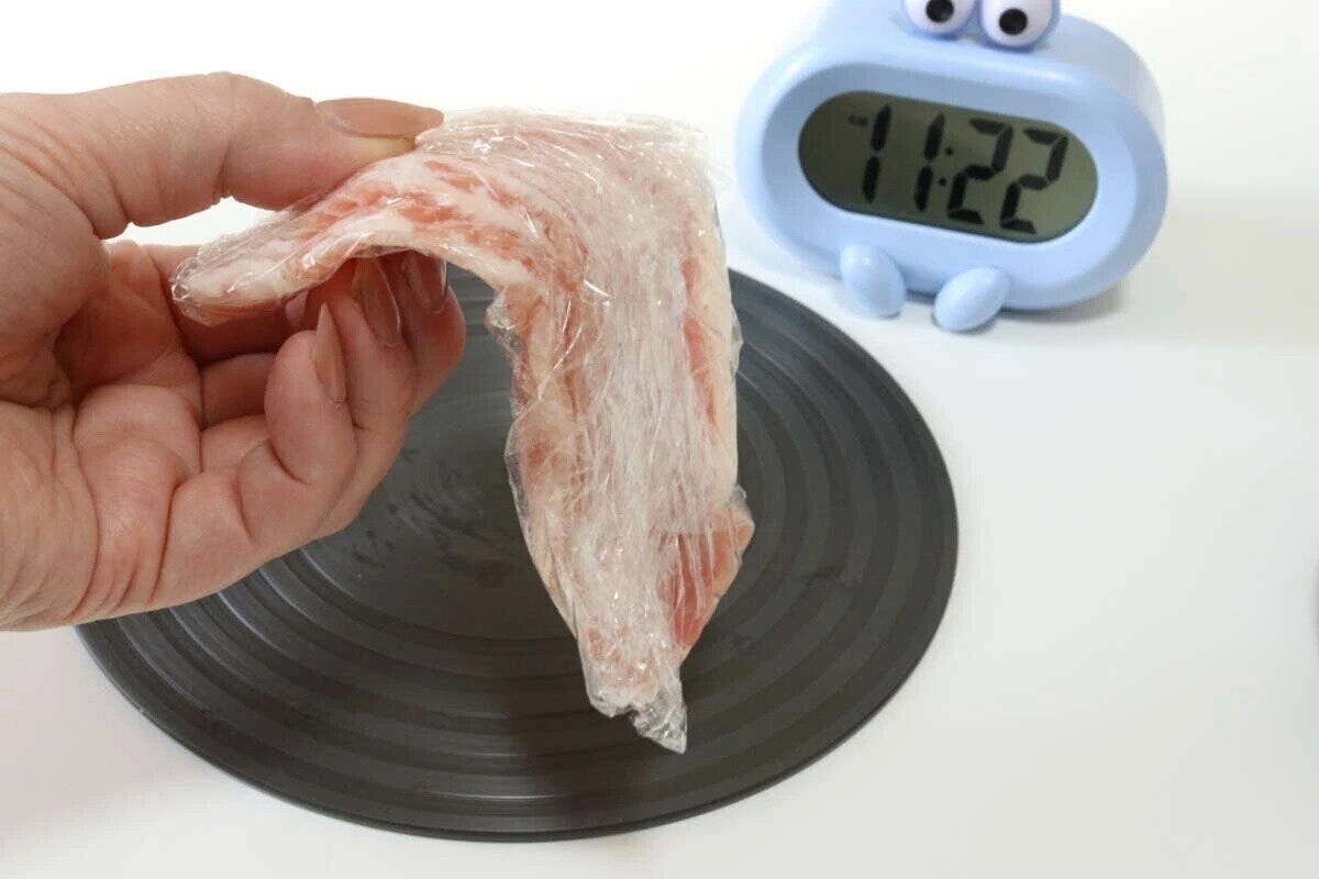 黒い解凍プレートの上にラップされた肉とデジタル時計