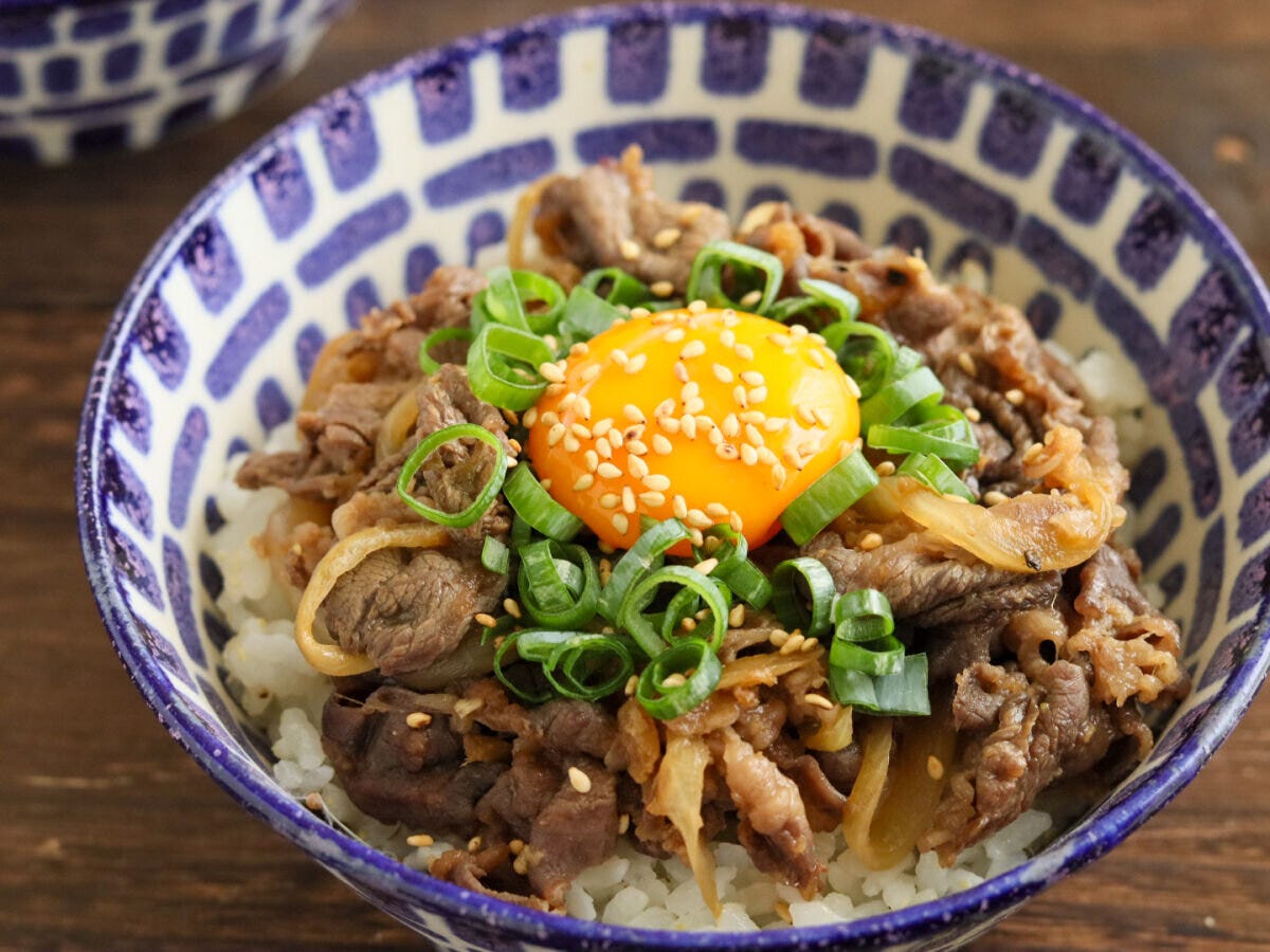 模様の丼にご飯と炒めた牛肉、卵黄、小ねぎ、白いりごまが盛られたスタミナ丼 模様の丼にご飯と炒めた牛肉、卵黄、小ねぎ、白いりごまが盛られたスタミナ丼