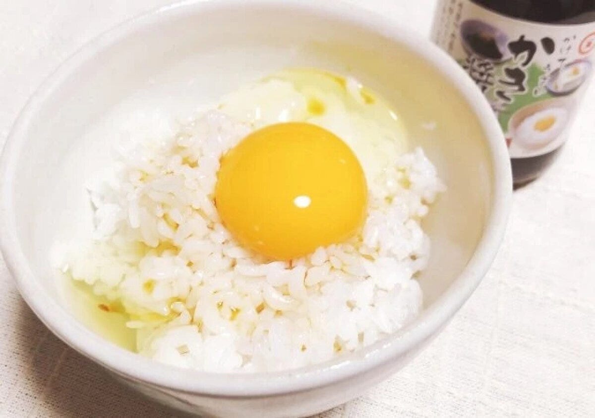 白いご飯の上に生卵が乗ったたまごかけご飯と、奥にかき醤油のボトル 白いご飯の上に生卵が乗ったたまごかけご飯と、奥にかき醤油のボトル