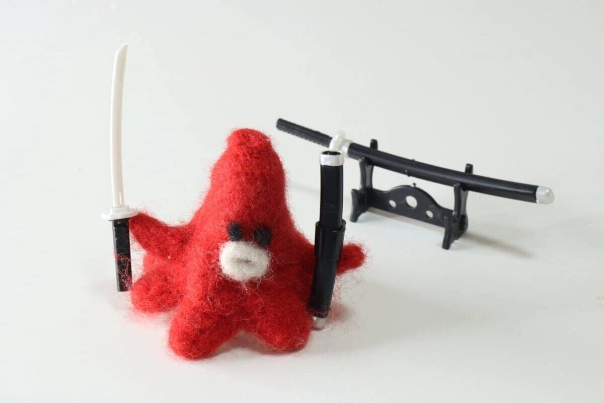 赤いぬいぐるみに白い長刀を持たせ刀掛けに飾った刀を並べた写真 赤いぬいぐるみに白い長刀を持たせ刀掛けに飾った刀を並べた写真