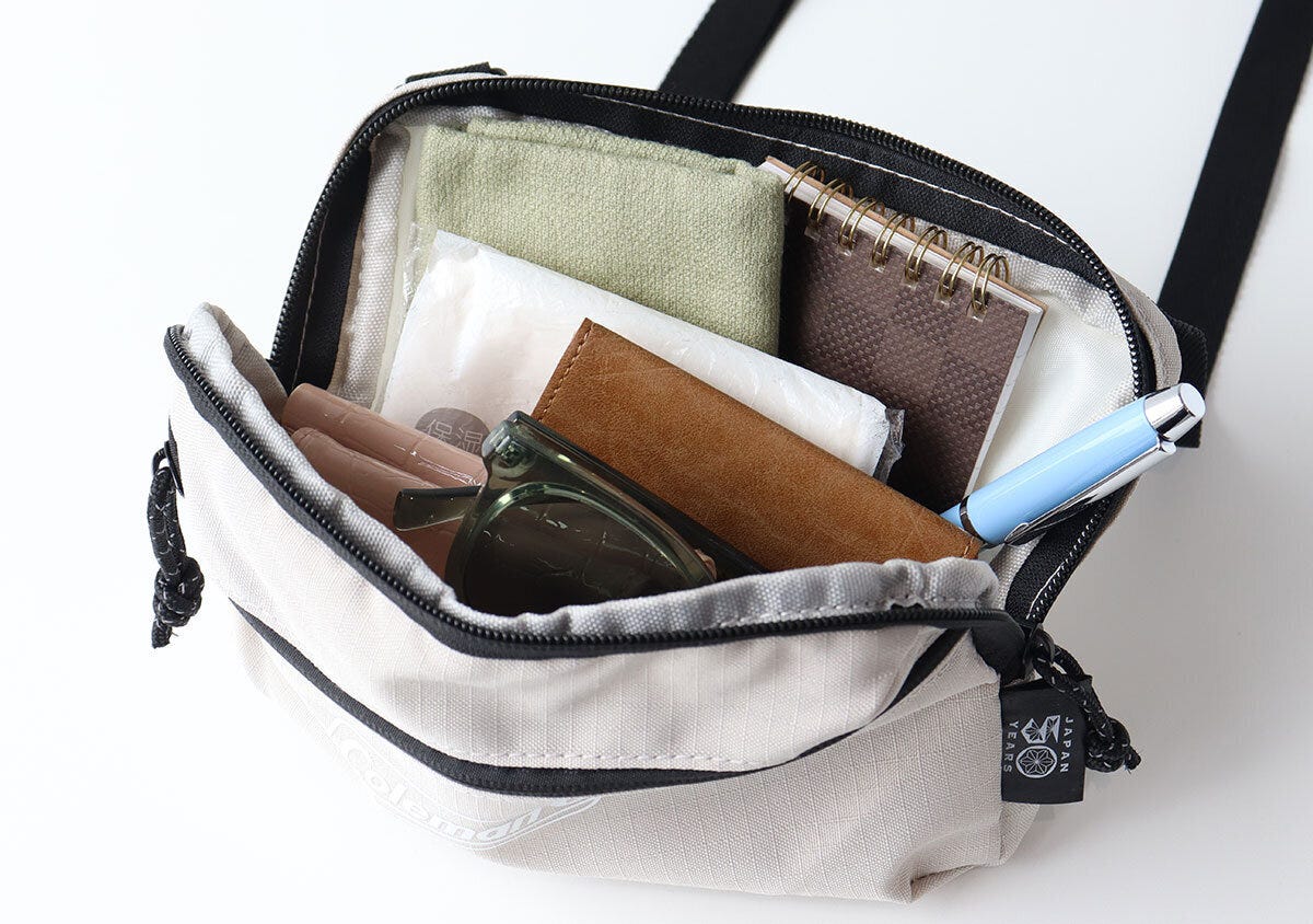 Colemanミニショルダーの中身。緑のタオル・茶色の財布・グリーンのサングラス・茶色のリングノート・青いペンが入っている