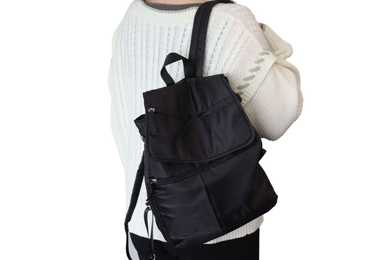 白いニットを着た女性が黒いリュックを肩にかけている様子