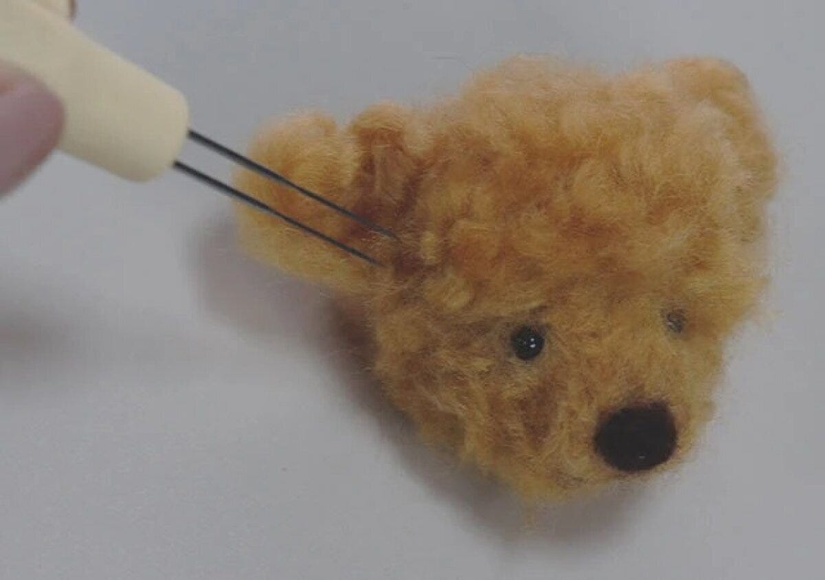 羊毛フェルトで作られたクマの顔の耳部分をニードルで刺している手元 羊毛フェルトで作られたクマの顔の耳部分をニードルで刺している手元