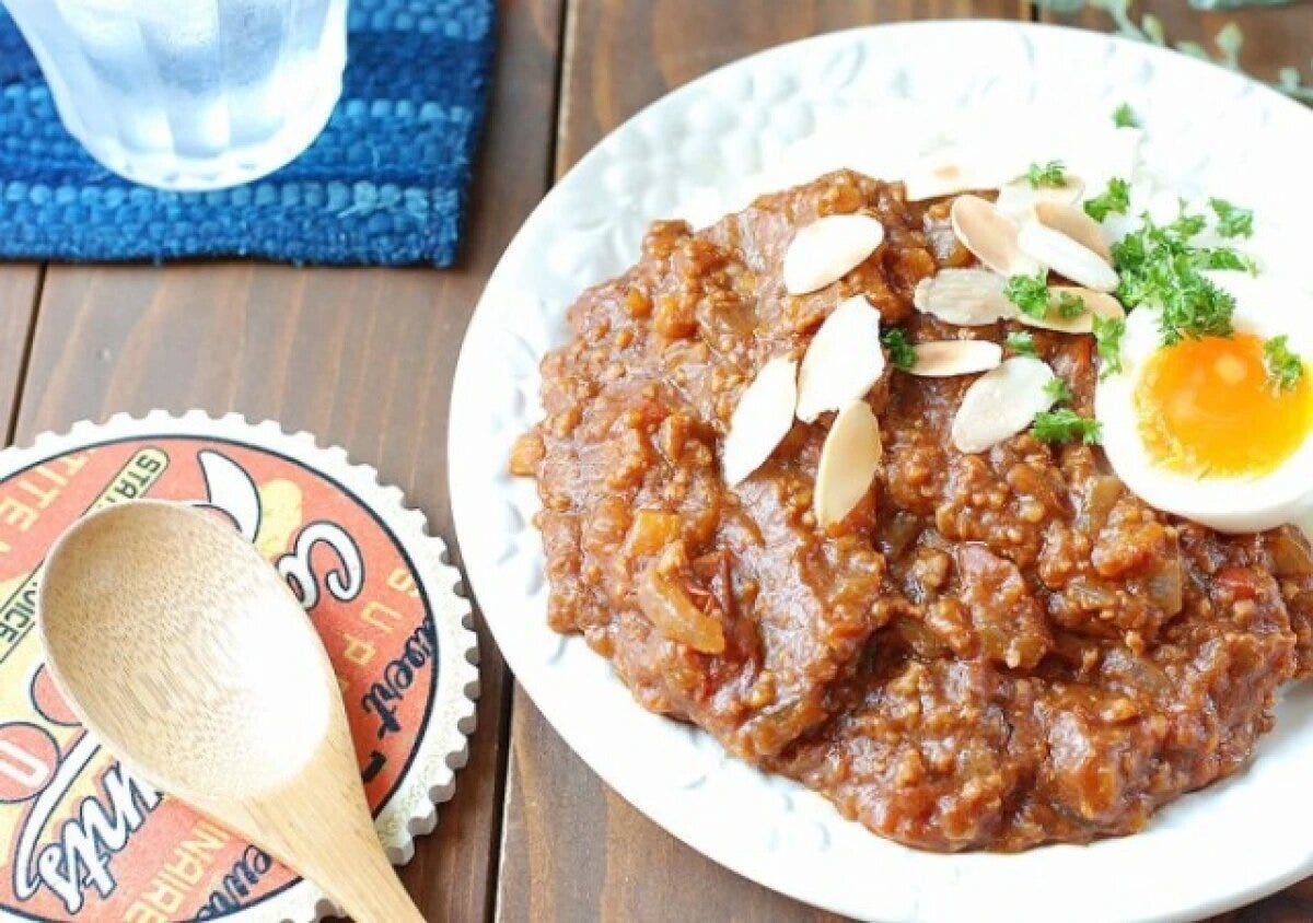 白い丸皿に盛られたキーマカレーとご飯、半熟のゆで卵、スライスアーモンドとパセリのトッピング、木製スプーン添え