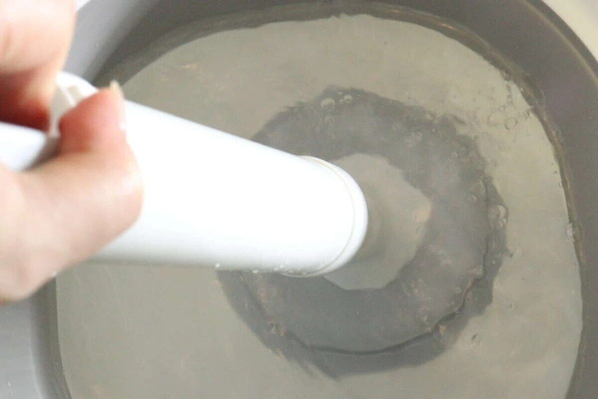 トイレの便器に白いパイプクリーナーを差し込んでいる様子